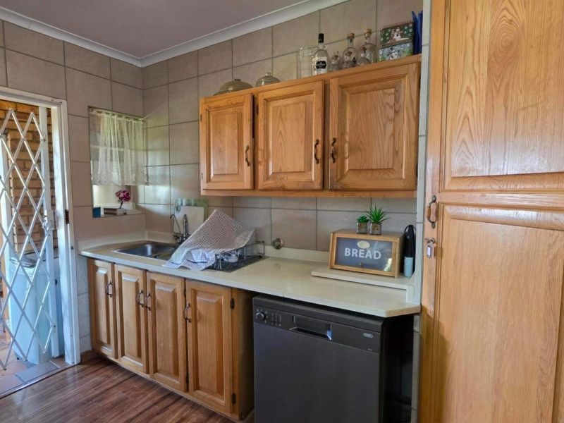 A functional kitchen featuring wooden cabinetry, tiled backsplash, and laminate flooring, with direct access to an outdoor area through a security gate.
