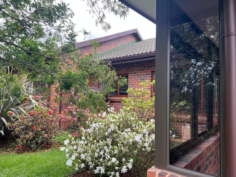 A view of the rear exterior featuring face brick walls, tiled roofing, and established garden landscaping with mature shrubs.
