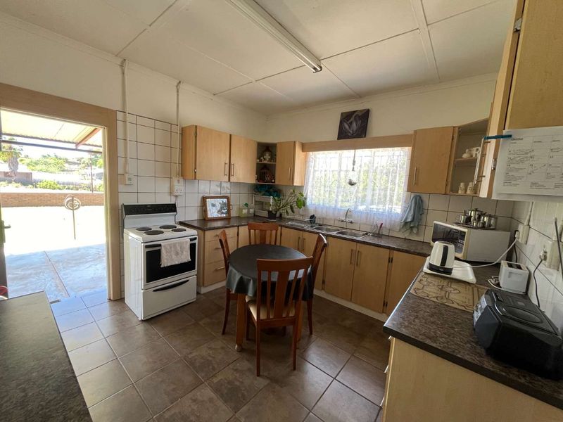 A functional kitchen featuring light wood cabinetry, tiled flooring, and a tiled backsplash, with direct access to an outdoor patio area.