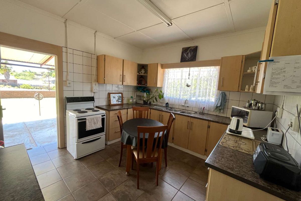 A functional kitchen featuring light wood cabinetry, tiled flooring, and a tiled backsplash, with direct access to an outdoor patio area.