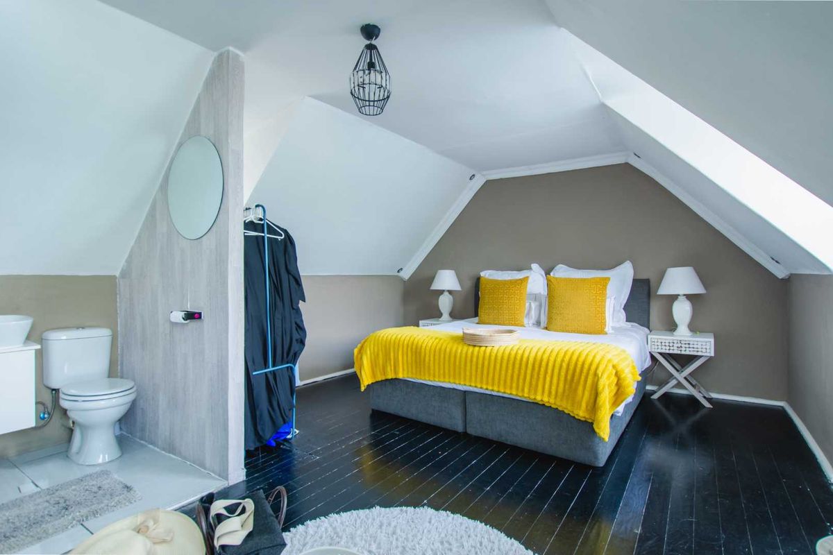 Attic-style bedroom featuring sloped ceilings, dark timber flooring, and an integrated open-plan en-suite bathroom with a toilet and vanity.