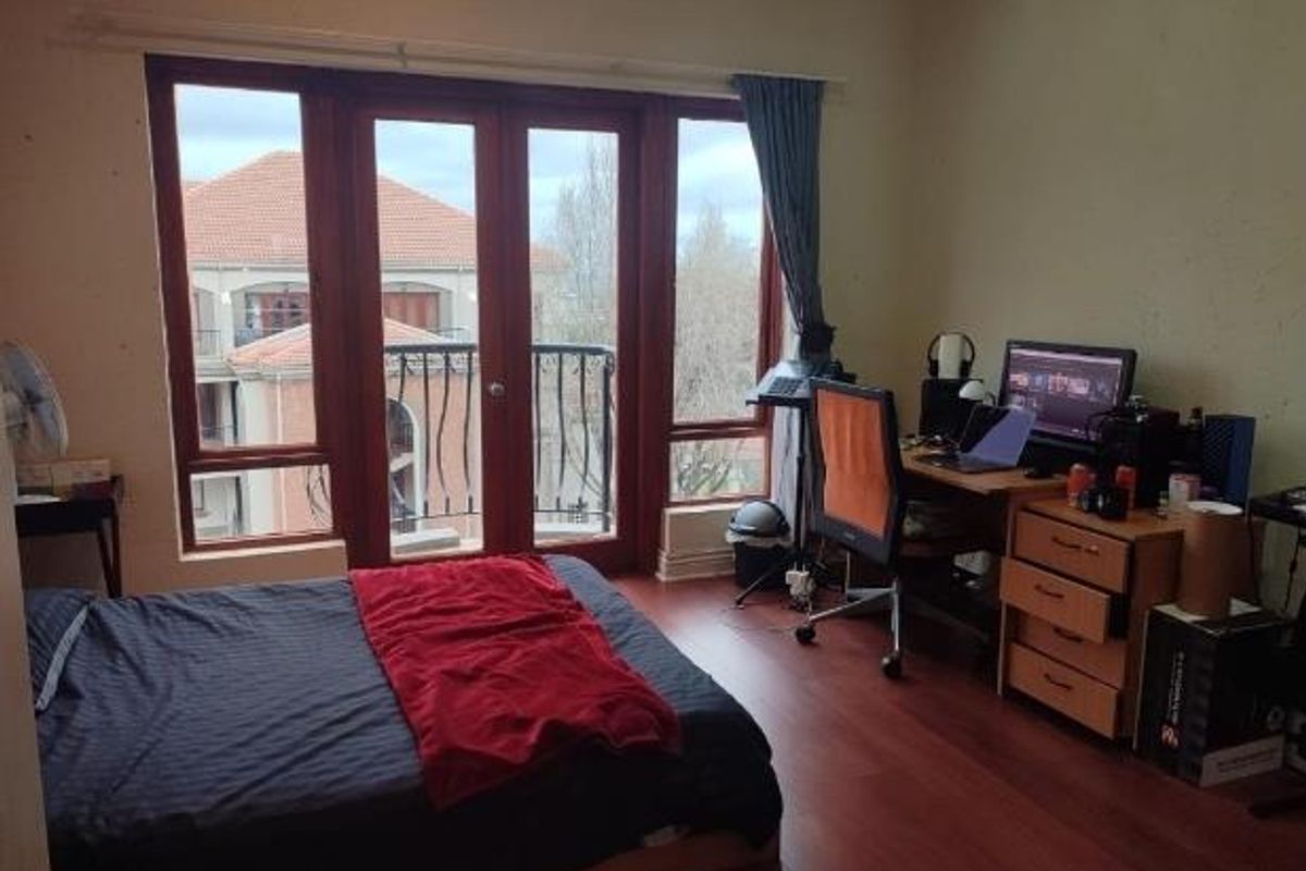 A bedroom featuring laminate flooring, large wooden-framed windows, and a glass door leading to a private balcony.