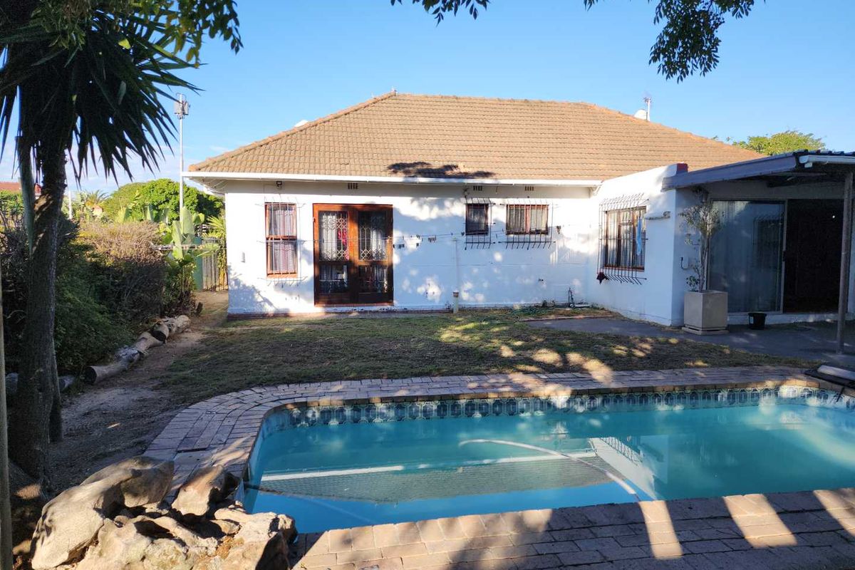 Rear view of the house featuring a swimming pool, paved pool surround, and a covered patio area with white exterior walls and tiled roof.