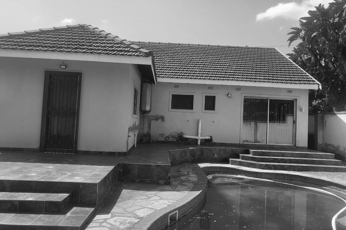 Rear exterior view of the house featuring a tiled patio, sliding door access, and a swimming pool with surrounding tiled decking.
