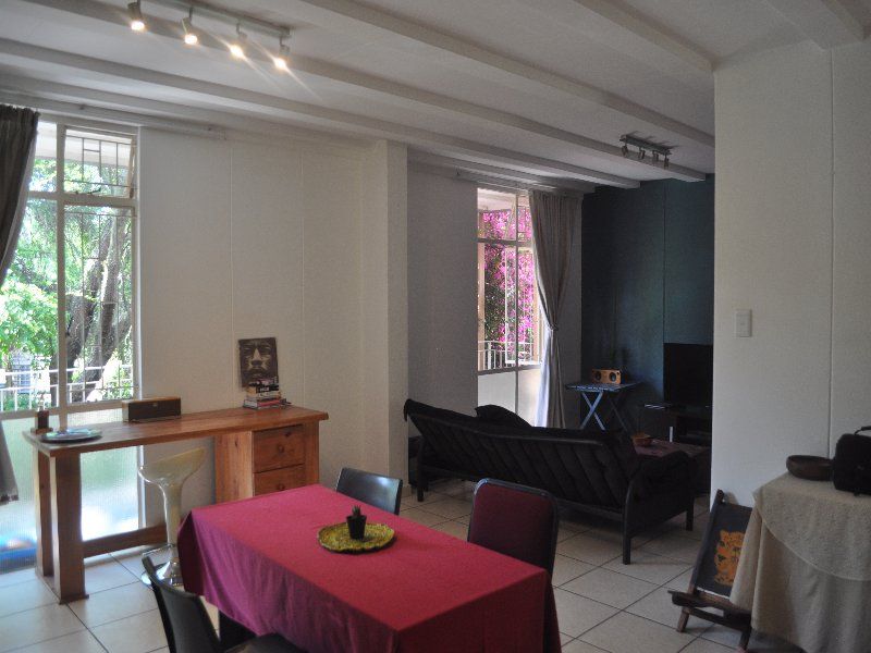 Spacious open-plan living and dining area featuring tiled flooring, exposed ceiling beams, and large windows providing natural light and garden views.