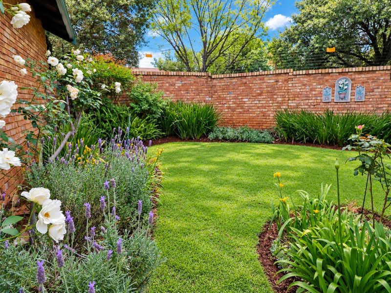 A well-maintained private garden featuring a lush green lawn, established flower beds, and a secure brick boundary wall with electric fencing.