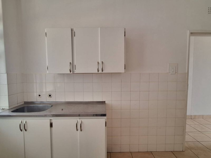 A compact, empty kitchen featuring a stainless steel sink, white built-in cabinetry, and tiled backsplash, offering a blank canvas for renovation.