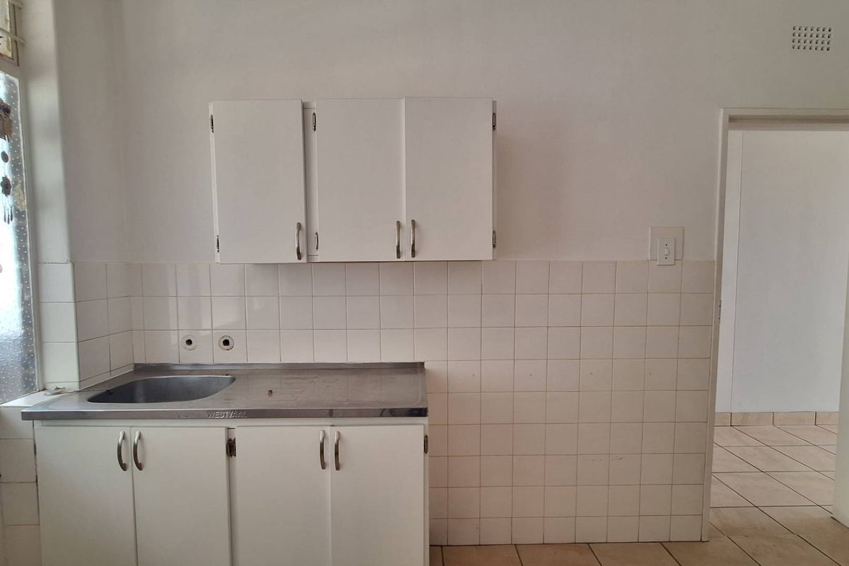 A compact, empty kitchen featuring a stainless steel sink, white built-in cabinetry, and tiled backsplash, offering a blank canvas for renovation.