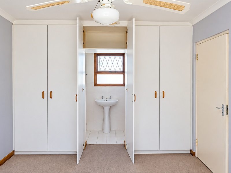 A bedroom featuring built-in wardrobes and an integrated vanity area with a pedestal basin and leaded glass window.