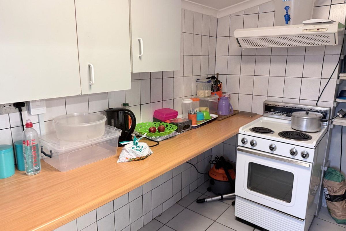 A functional kitchen featuring tiled walls, laminate countertops, and a freestanding electric stove with an overhead extractor fan.