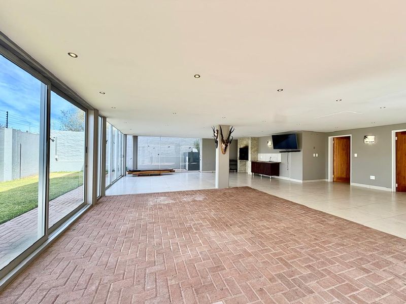 Spacious open-plan living area featuring large sliding glass doors, built-in bar, indoor braai, and a mix of tiled and brick flooring.