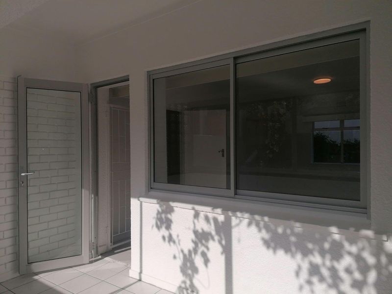 A bright, covered patio area featuring tiled flooring, a modern sliding glass window, and a secure entrance door.