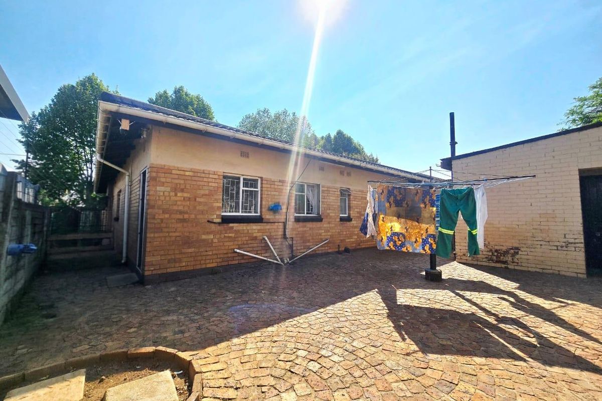 Rear exterior view of the house featuring a brick facade, security bars on windows, and a paved courtyard area.