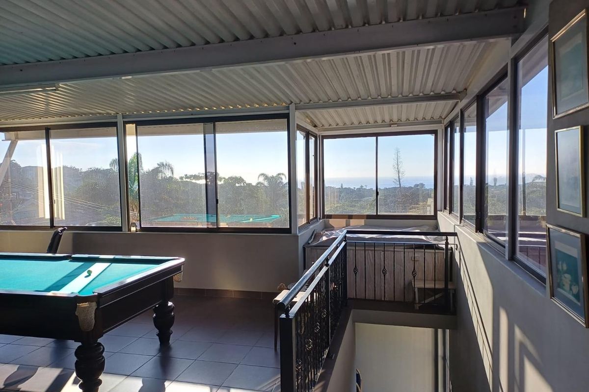 An elevated entertainment area featuring large windows with scenic views, tiled flooring, and a metal roof structure, overlooking a lower level.