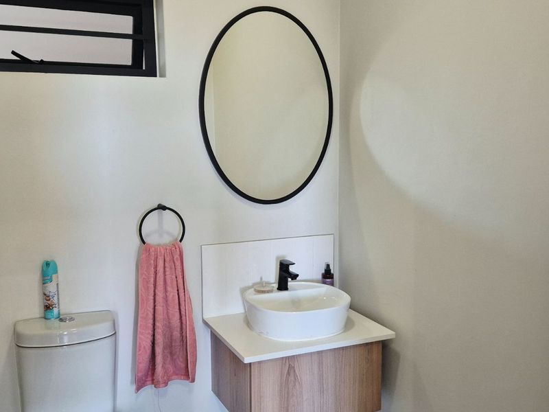 A modern bathroom featuring a vanity cabinet with a vessel sink, black fixtures, and an oval mirror.