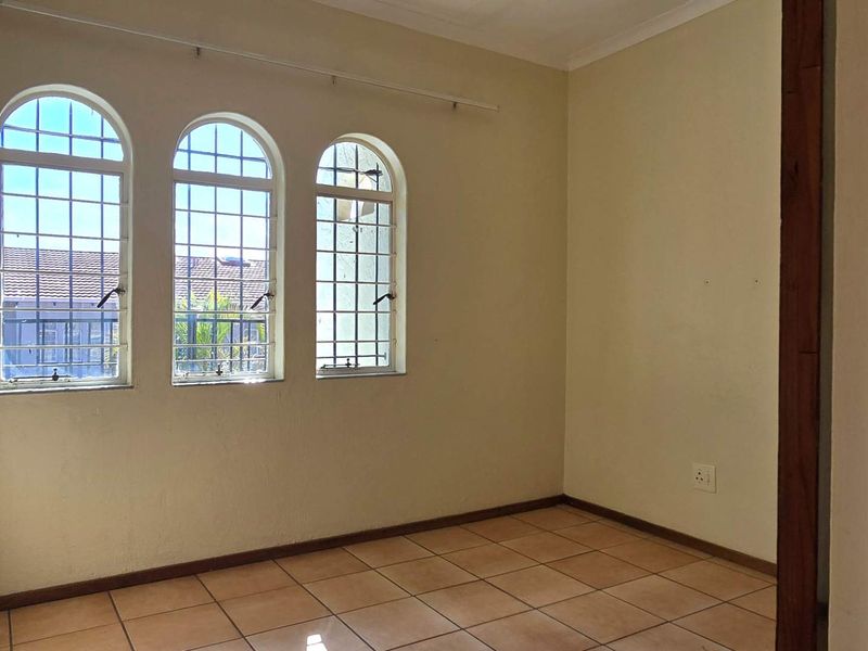 An empty bedroom featuring tiled flooring and three arched windows with security bars, offering a blank canvas for personalization.