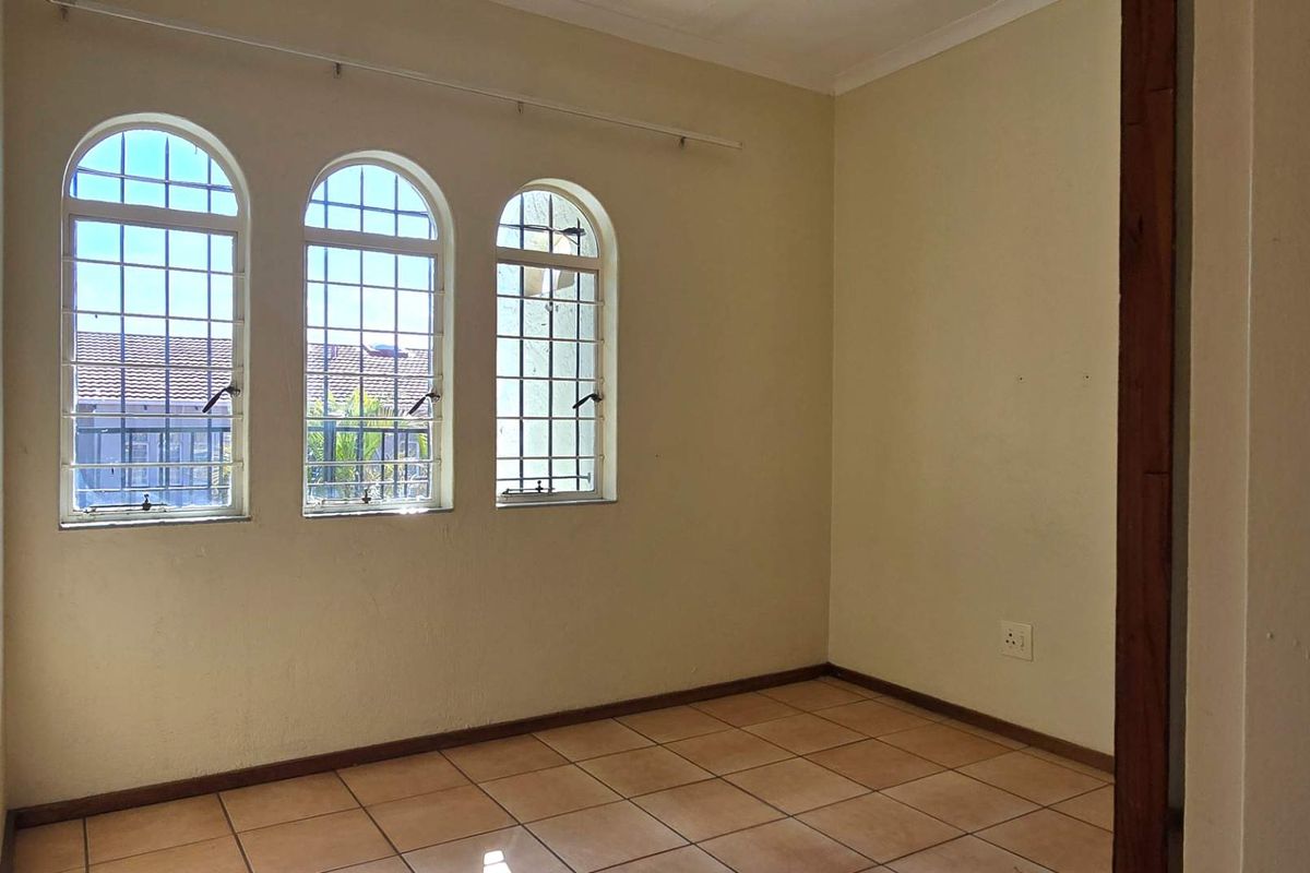 An empty bedroom featuring tiled flooring and three arched windows with security bars, offering a blank canvas for personalization.