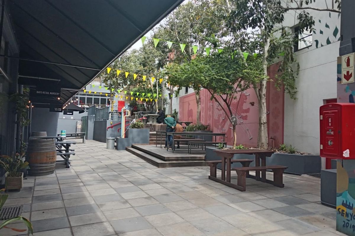 An outdoor paved courtyard area featuring raised timber decking, built-in planters, and a retractable awning, suitable for communal office use or break-out space.