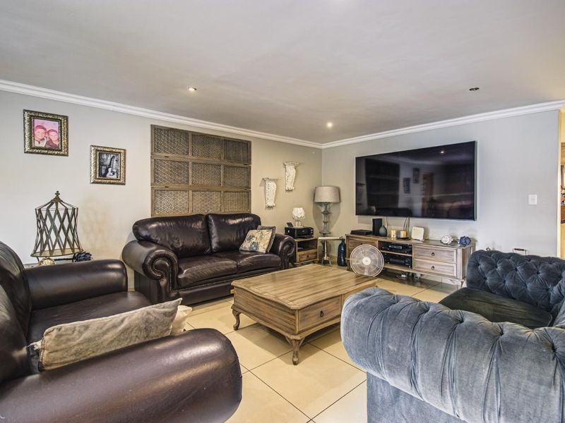 A spacious living room featuring neutral tiled flooring, recessed downlighting, and decorative crown molding, providing a comfortable and well-maintained area for relaxation.