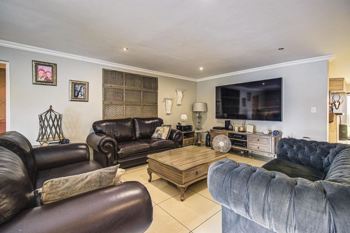 A spacious living room featuring neutral tiled flooring, recessed downlighting, and decorative crown molding, providing a comfortable and well-maintained area for relaxation.