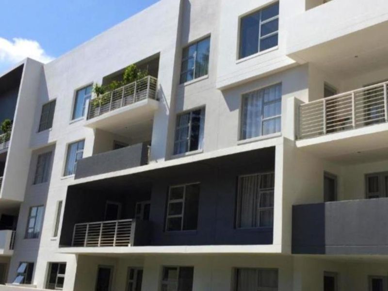 A modern apartment building exterior featuring multiple balconies with metal railings and large aluminium-framed windows.