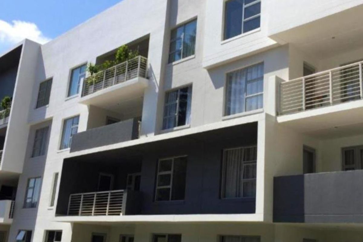 A modern apartment building exterior featuring multiple balconies with metal railings and large aluminium-framed windows.