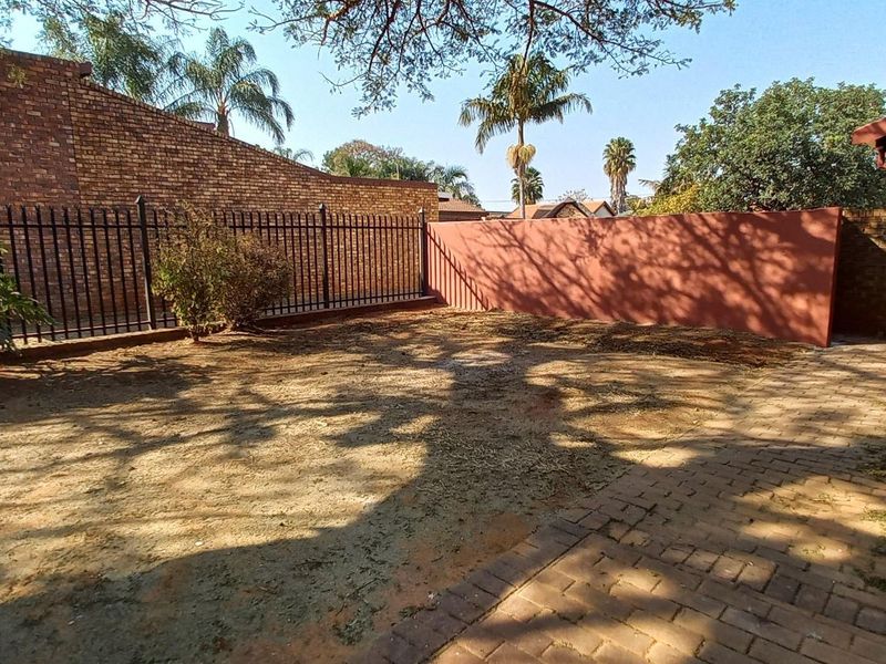 A private rear garden area featuring a paved patio, brick boundary walls, and metal security fencing.