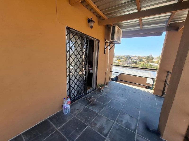 A covered balcony featuring tiled flooring, a security gate, and a wall-mounted air conditioning unit, offering an elevated view of the surrounding area.
