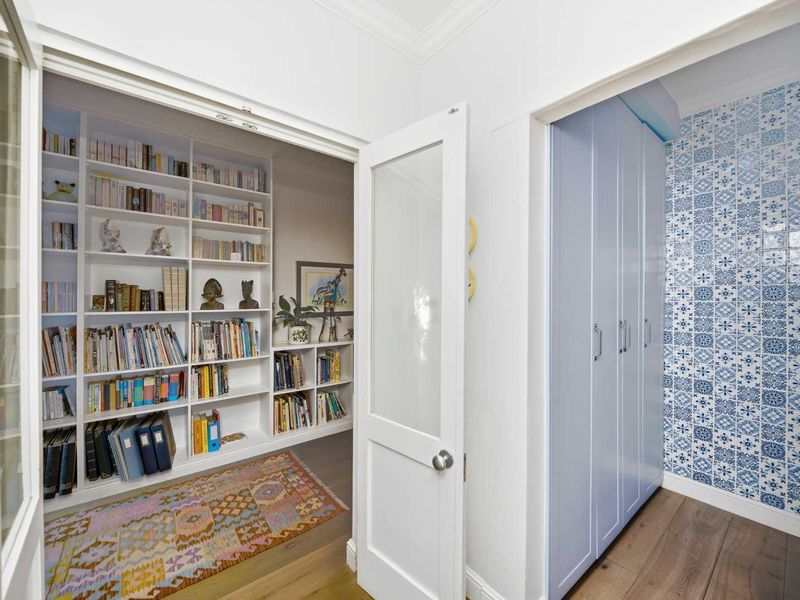 A bright hallway featuring built-in floor-to-ceiling bookshelves, timber flooring, and a storage area with decorative blue and white patterned wall tiles.