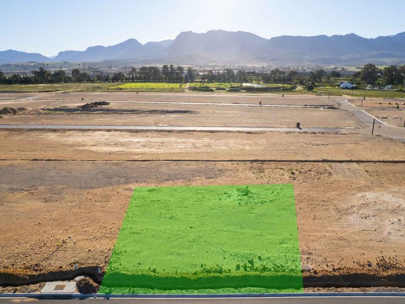 An aerial view of a vacant residential plot in a developing estate, featuring clear boundaries and surrounding landscape views.