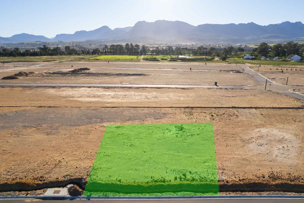An aerial view of a vacant residential plot in a developing estate, featuring clear boundaries and surrounding landscape views.