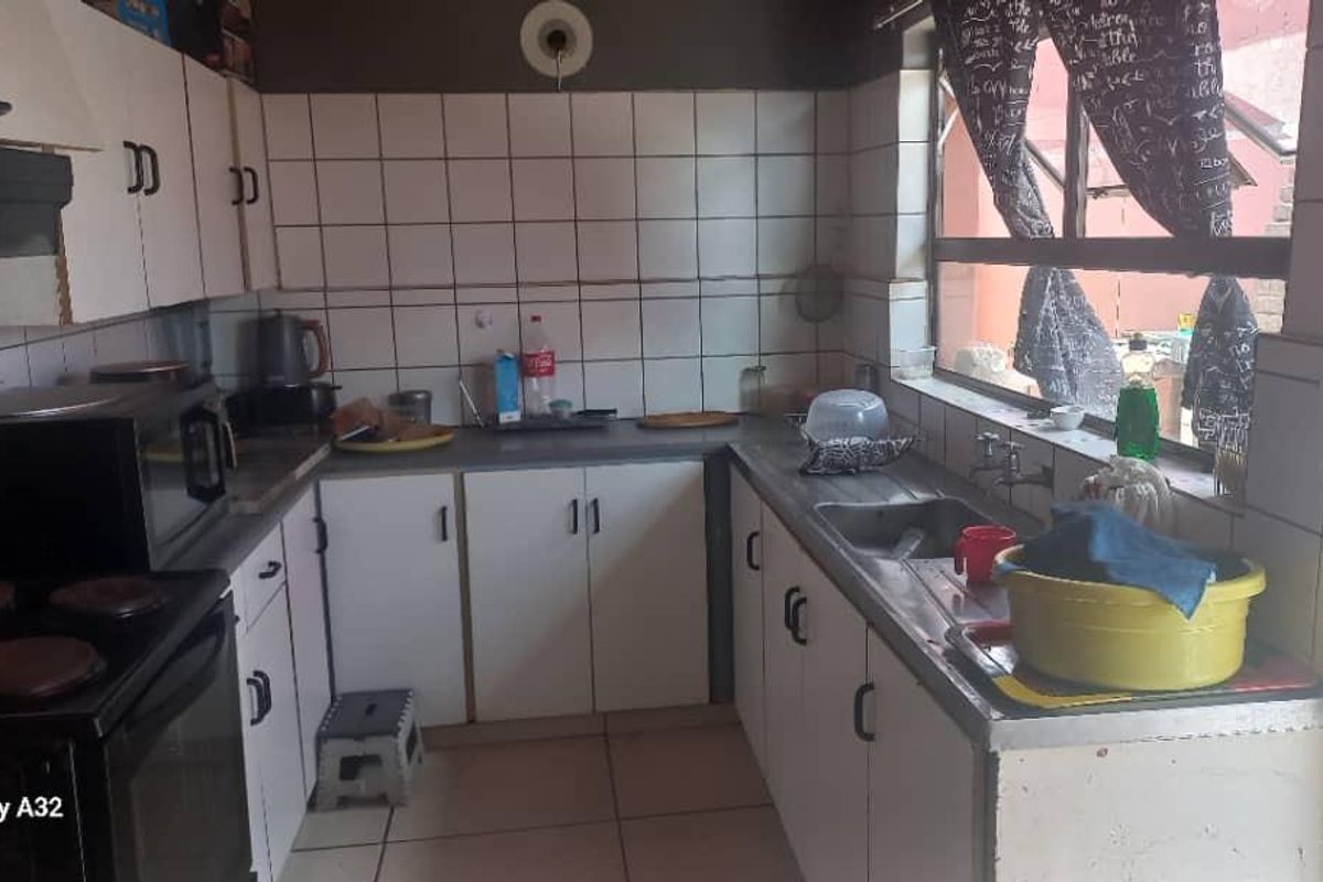 A compact kitchen featuring white cabinetry, tiled splashbacks, a built-in oven with extractor fan, and a stainless steel sink.