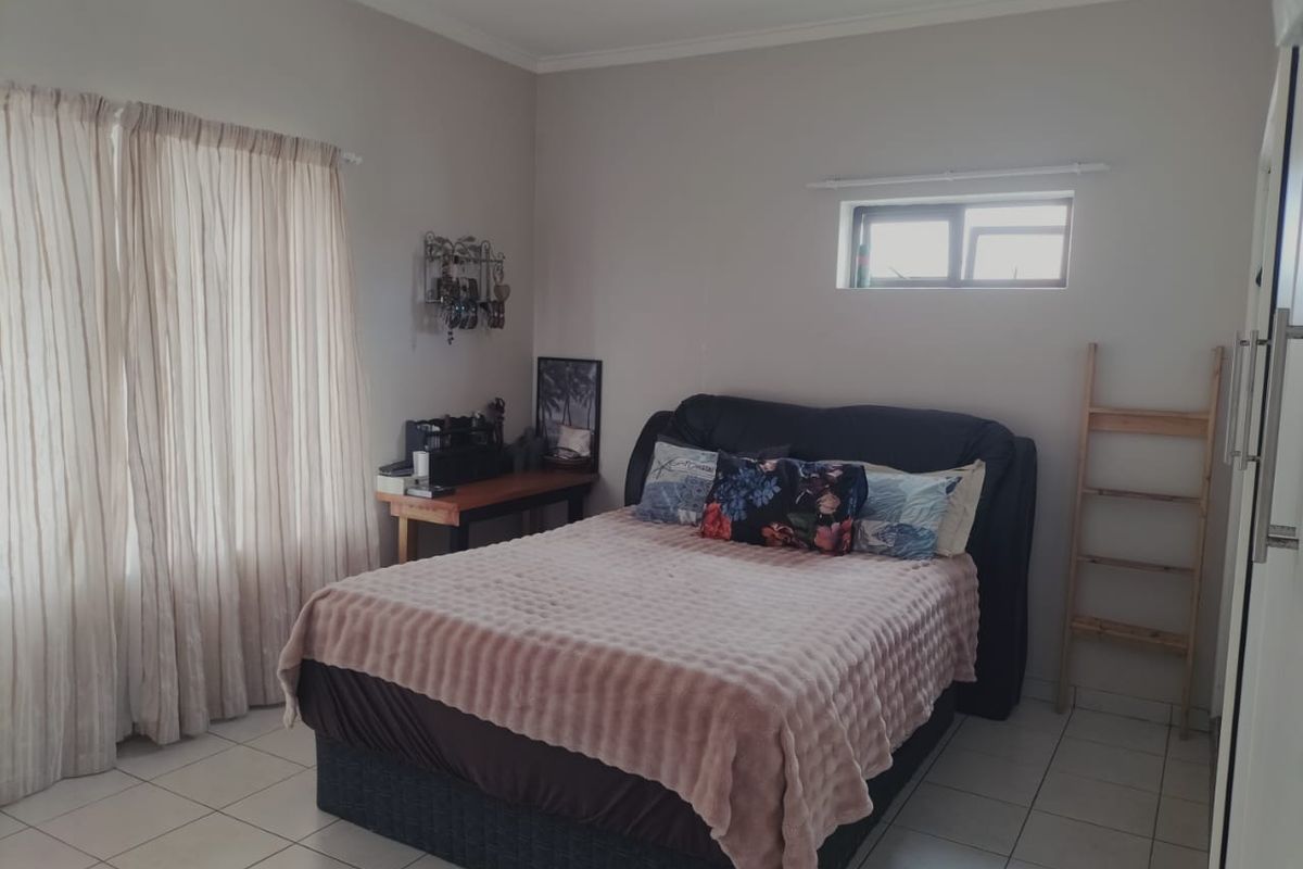 A well-lit bedroom featuring tiled flooring, neutral wall tones, and a combination of large and high-set windows for natural light.