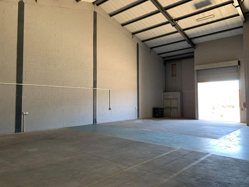 Spacious industrial warehouse unit featuring high ceilings, durable concrete flooring, exposed steel structural beams, and a large roller shutter door for easy access.