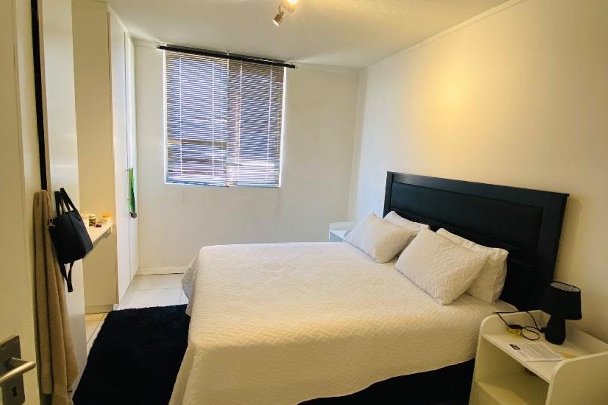 A functional bedroom featuring tiled flooring, built-in cupboards, and a window with fitted blinds.