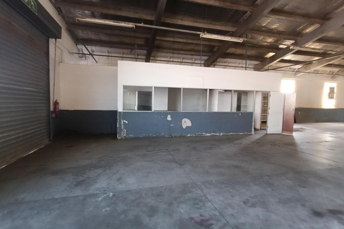 Spacious industrial utility area featuring high ceilings with exposed steel trusses, a large roller shutter door, and a partitioned office enclosure.