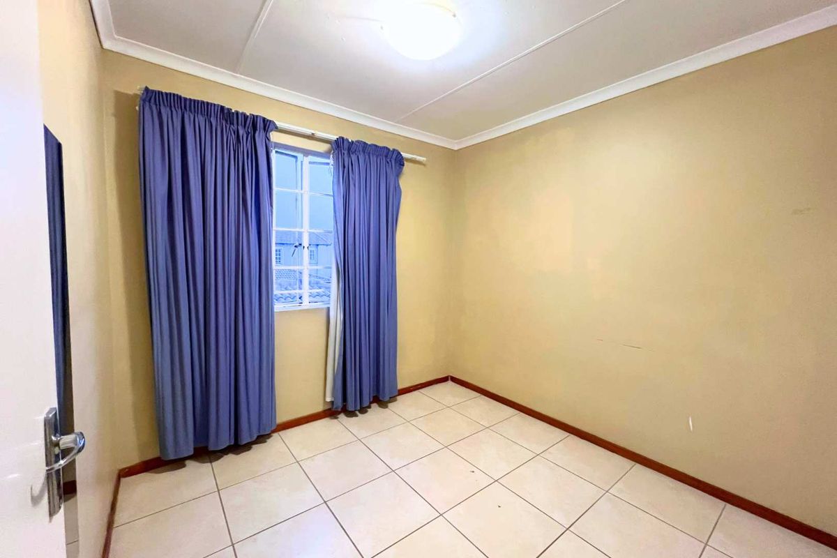 A vacant bedroom featuring neutral wall paint, tiled flooring, and a window with curtain tracks.