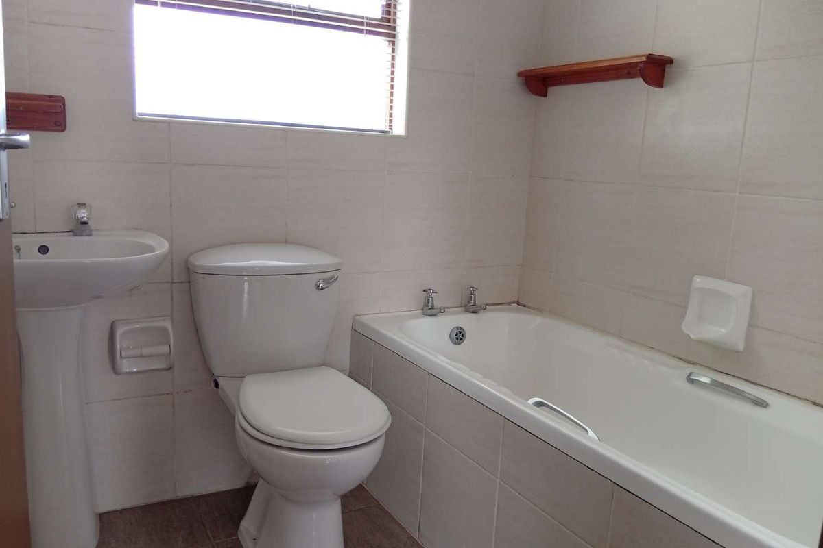 A functional bathroom featuring a pedestal basin, standard toilet, and a built-in bathtub with tiled walls and flooring.