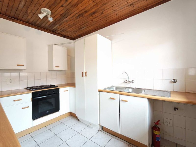A functional kitchen featuring built-in cabinetry, a hob, an oven, and a double sink with tiled splashbacks and a timber-paneled ceiling.