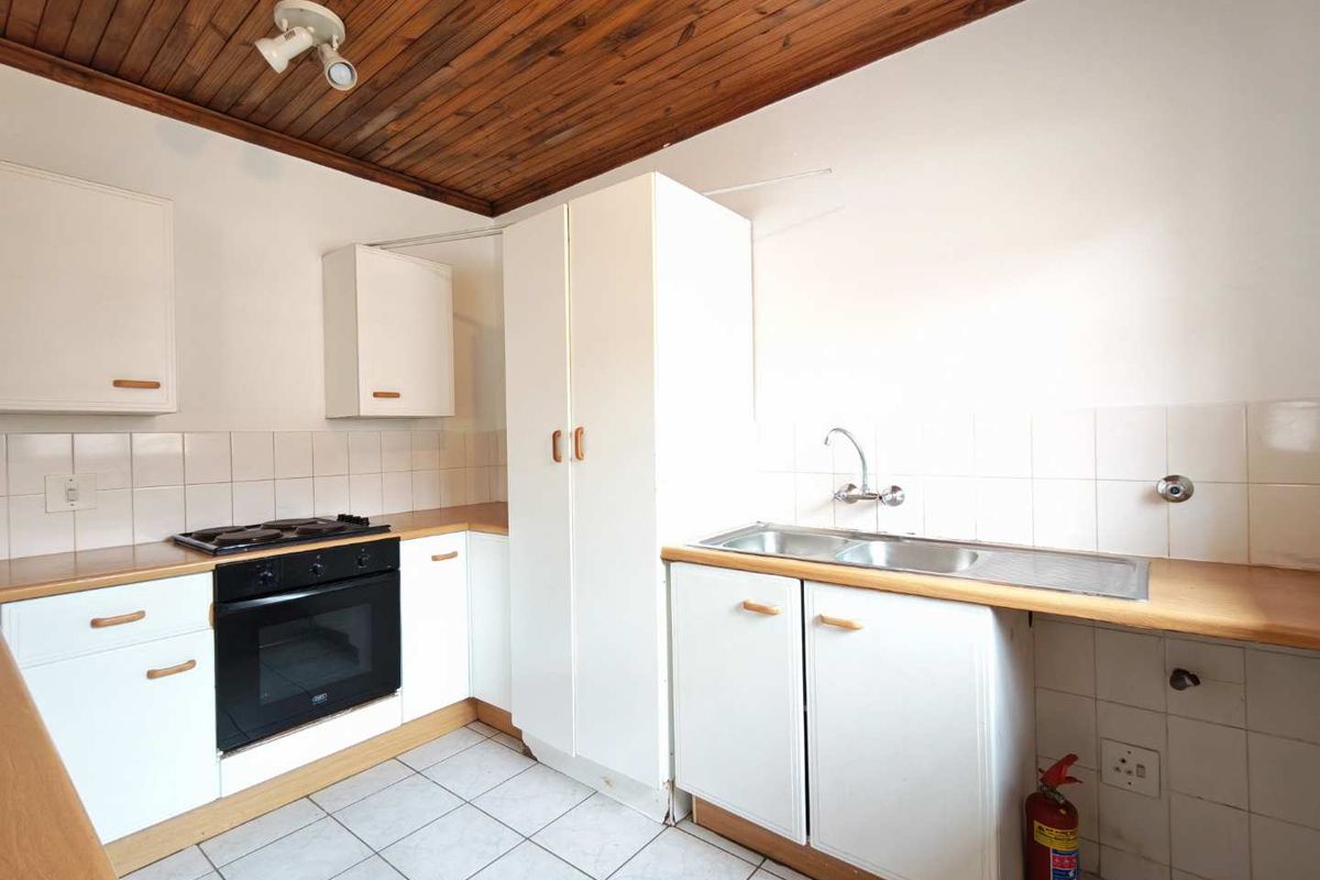 A functional kitchen featuring built-in cabinetry, a hob, an oven, and a double sink with tiled splashbacks and a timber-paneled ceiling.