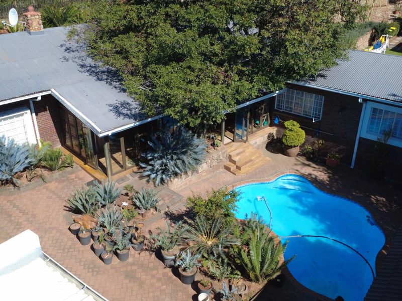 Aerial view of a residential property featuring a swimming pool, paved courtyard area, and brick building structure with a corrugated metal roof.