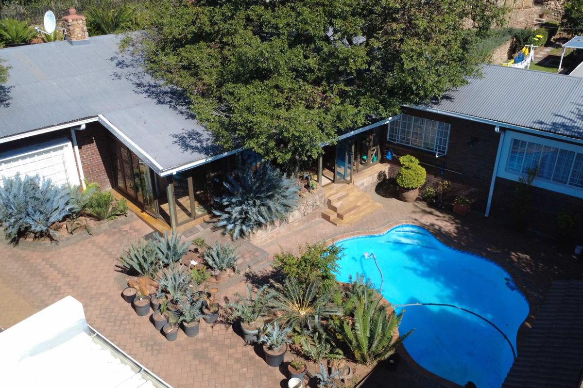 Aerial view of a residential property featuring a swimming pool, paved courtyard area, and brick building structure with a corrugated metal roof.