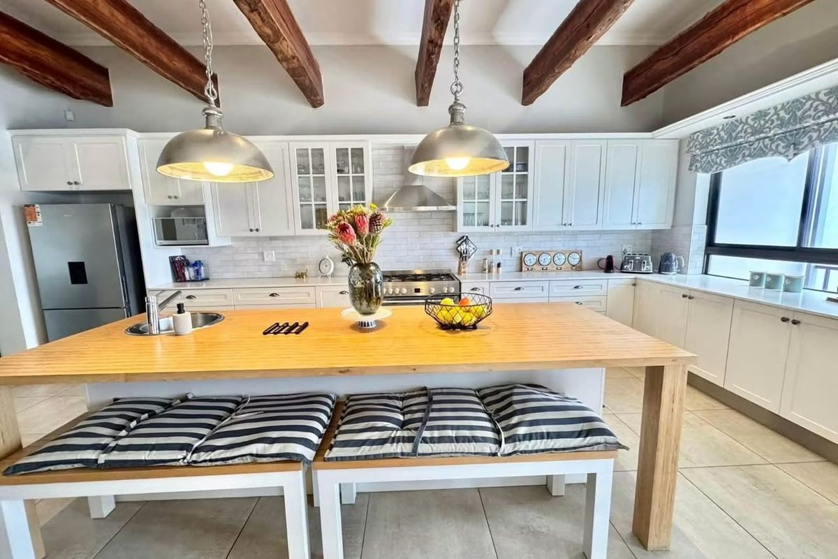 A well-appointed kitchen featuring white shaker cabinetry, subway tile backsplash, exposed timber ceiling beams, and a large central island with integrated seating.