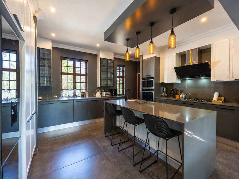 Modern, well-appointed kitchen featuring a large central island, stone countertops, integrated appliances, sleek cabinetry, and stylish pendant lighting.