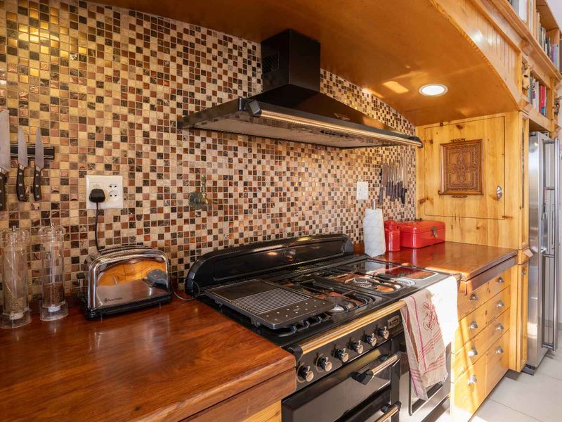A kitchen area featuring a gas range stove, extractor fan, mosaic tile backsplash, and wooden cabinetry with integrated wooden countertops.