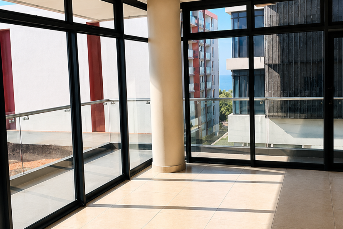 Bright and spacious living area featuring floor-to-ceiling windows, neutral tiled flooring, and a central structural column, offering an open and airy atmosphere.