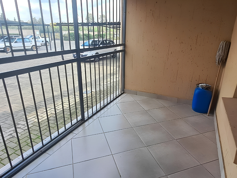 A covered patio area featuring tiled flooring, textured walls, and a secure metal gate overlooking the parking area.