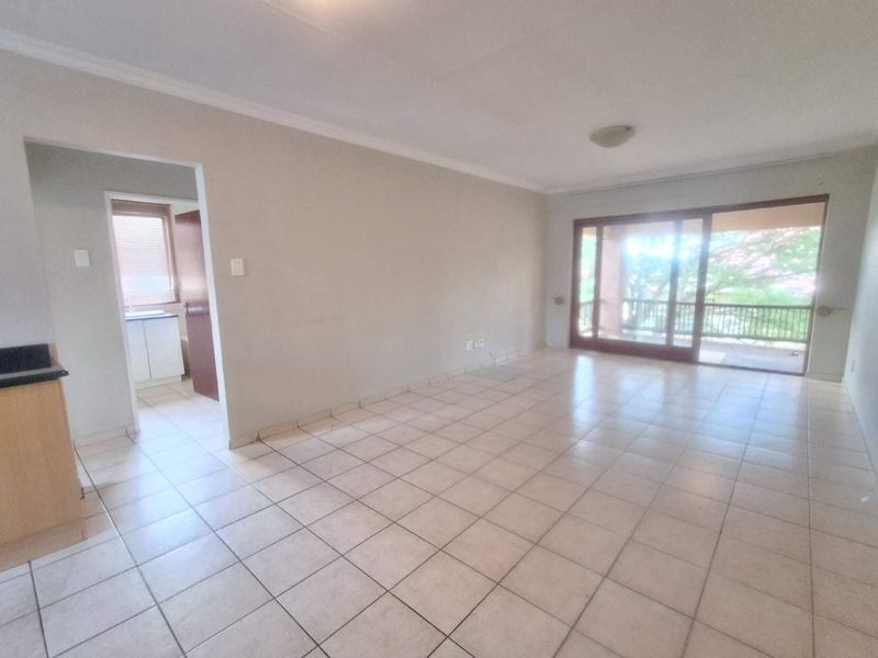 Spacious open-plan living area featuring tiled flooring, neutral walls, and large sliding glass doors providing access to an outdoor balcony.