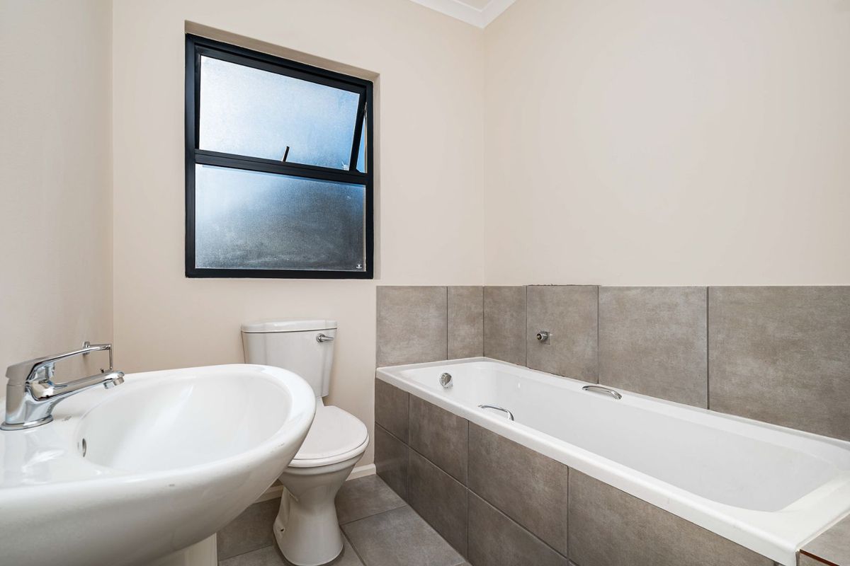A clean, functional bathroom featuring a white pedestal basin, a standard toilet, and a tiled bathtub with neutral wall and floor finishes.