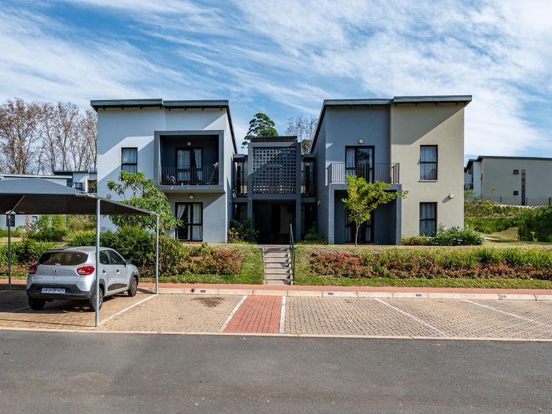 Front elevation of a modern apartment complex featuring paved parking, carports, and private balconies with a central decorative breeze block architectural feature.